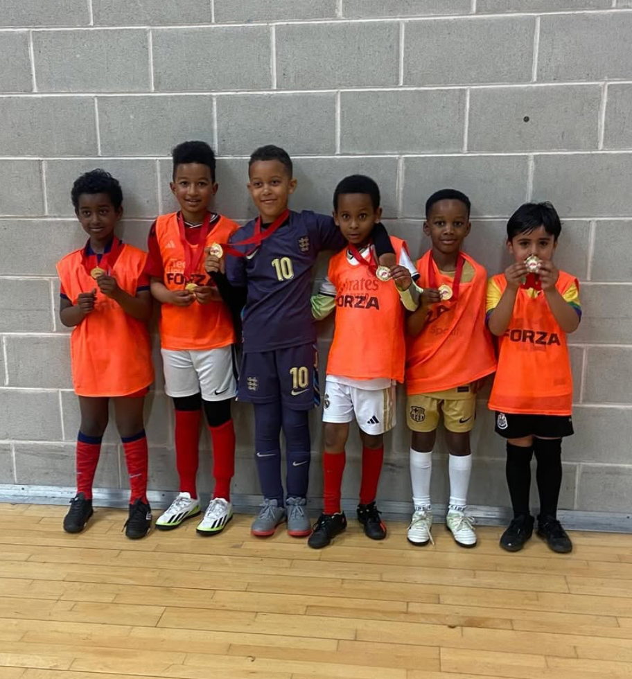 Children football players in Soccer Inclusion training bibs celebrating with medals after Birmingham youth tournament